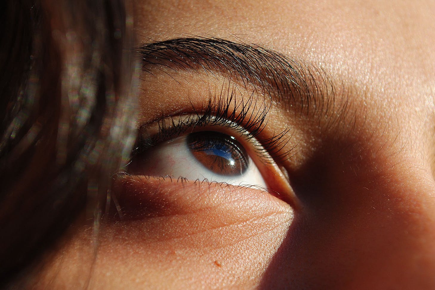 Someone looks up in the sunshine, showing their excellent eyelash extensions.